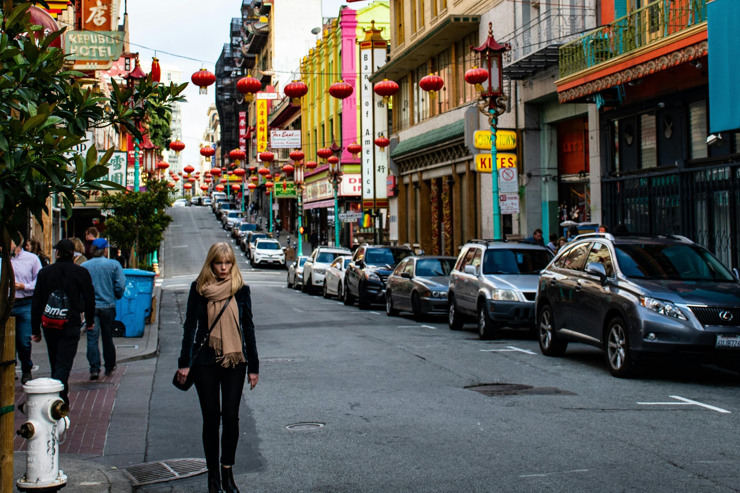 Vibrant Chinatown street featuring red lanterns, people, and parked cars on a bright day.