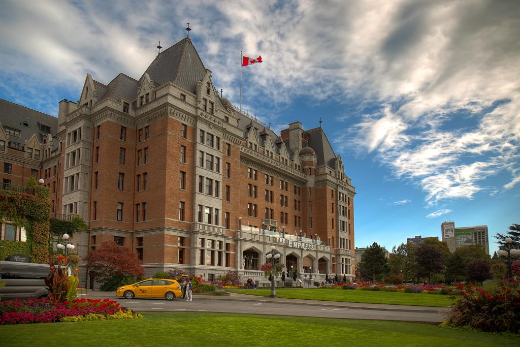 Historic Empress Hotel in Victoria, Canada under vibrant blue sky with colorful gardens and Canadian flag.