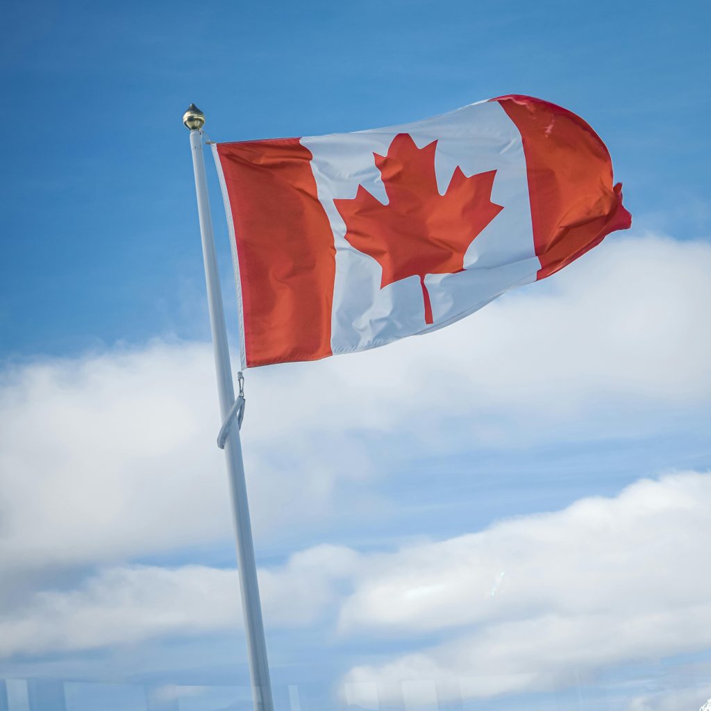 Canadian flag gracefully waving against a bright blue sky with fluffy clouds.
